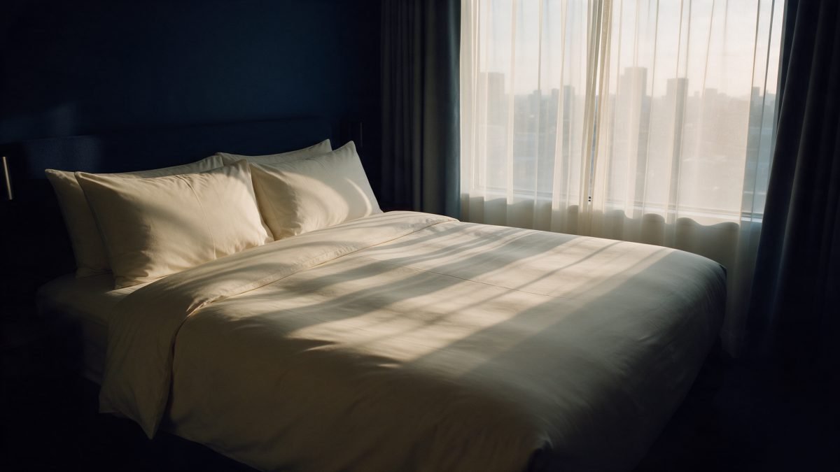 A calm hotel room at dawn with soft light through sheer curtains and a hazy skyline beyond
