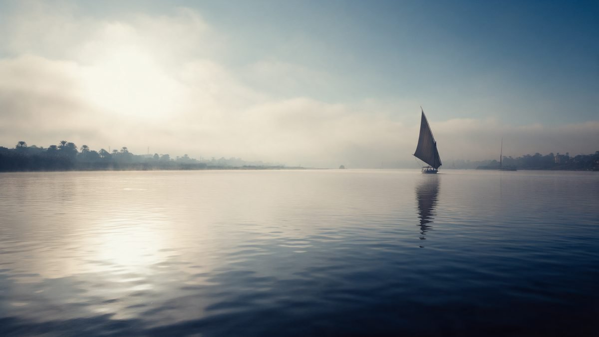 A cool winter morning on the Nile with a distant felucca sail catching soft golden light