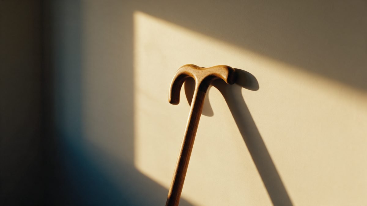 A simple wooden walking stick leaning against a sunlit cream wall