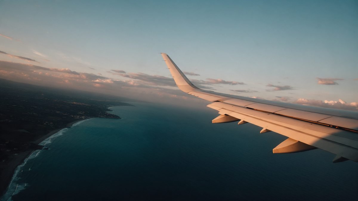 An aircraft wing gliding above a golden-hour Mediterranean coastline